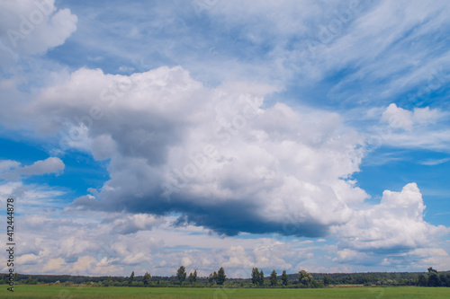 Picturesque summer landscape with white fluffy summer clouds on blue marvelous sky view background. Green meadow stock photo.