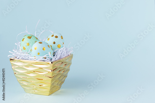 Easter eggs with gold dots in luxury golden bowl on blue background, copy space.