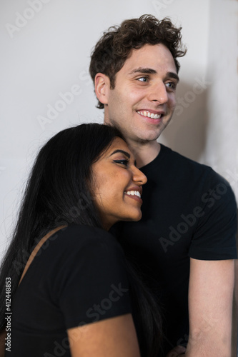 smiling multiethnic young couple with black clothes looking out the window hugging each other.