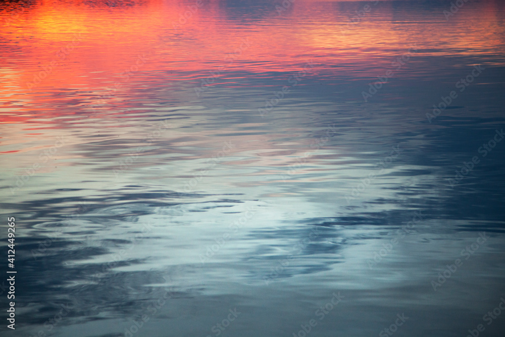 Background with reflection of the sunset on the sea surface. Abstract reflection of the sky in the blurred background of water