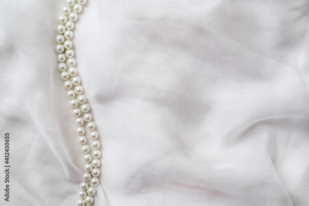 A necklace of pearls lies on a white cloth
A necklace of pearls lies on a white cloth