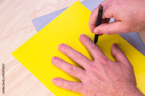 concept making an Easter bunny with your own hands a person circles his palm with a marker on a yellow piece of paper