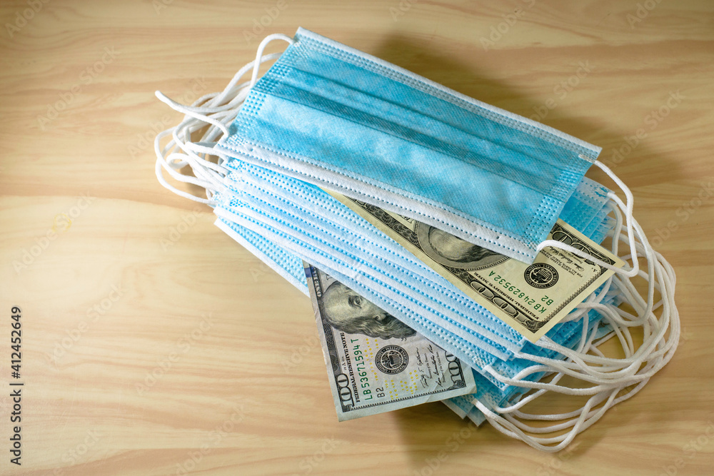 the concept of coronavirus and business a stack of medical masks lies on the table among the masks are hundred dollar bills the concept of coronavirus and business a stack of medical masks lies on the table among the masks are hundred dollar bills
