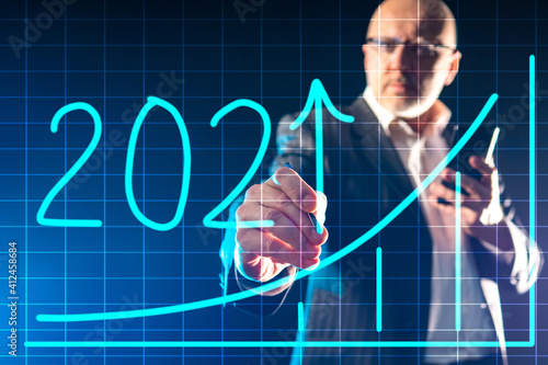A favorable forecast for 2021. A man draws an increasing graph with the number 2021. Economic growth. A positive Outlook for next year. © Grispb
