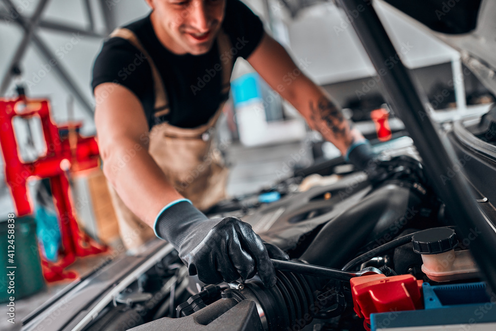 Cropped image of handsome mechanic in uniform is working in auto service. Car repair and maintenance. Cropped image of handsome mechanic in uniform is working in auto service. Car repair and maintenance.