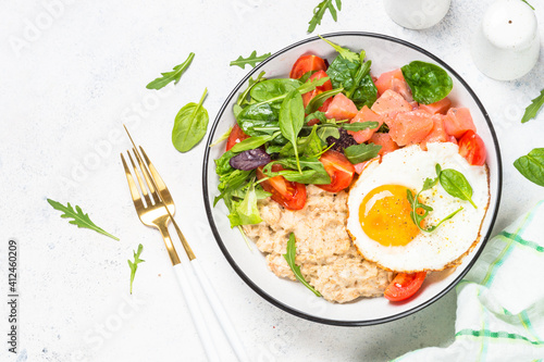 Savory breakfast. Oatmeal porrige with salted salmon, egg and fresh salad. Healthy food, balanced nutrition. Top view on white table.