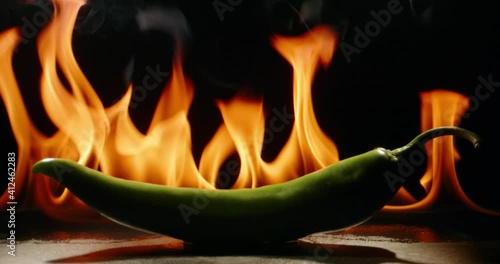Close up shot of green chili pepper burning in fire. Hot green pepper in flames.
