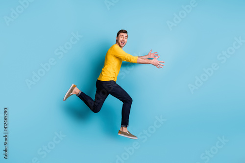 Full length profile portrait of cheerful carefree guy run arms catching good mood isolated on blue color background