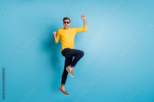 Full size profile photo of impressed handsome guy jumping fists up celebrate isolated on blue color background