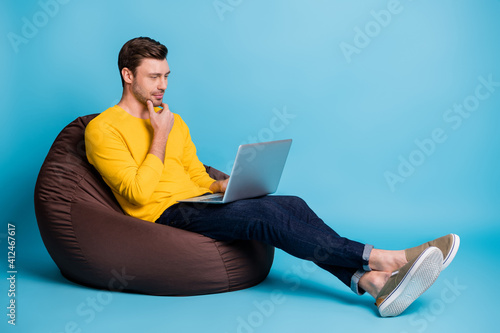 Full length profile portrait of positive man hand on chin use laptop sit in soft chair isolated on blue color background