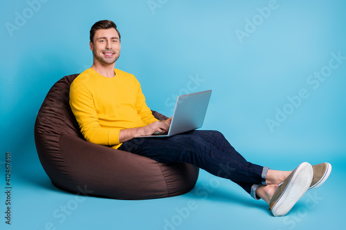 Portrait of attractive cheerful guy sitting in bag chair typing writing email isolated over bright blue color background