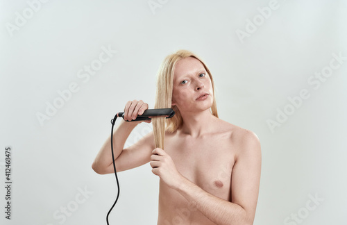 Young caucasian blond man applying hair straightener