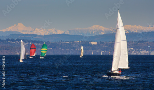 Multiple sailboats racing together towards the finish line in Tacoma's Commencement Bay, all with lots of wind in their colorful spinnakers.