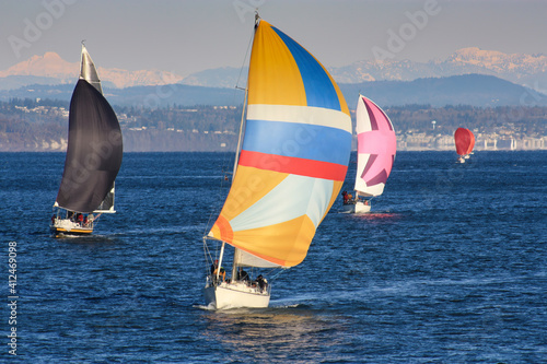 Multiple sailboats racing together towards the finish line in Tacoma's Commencement Bay, all with lots of wind in their colorful spinnakers.