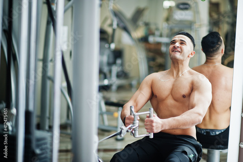 Muscular arab man training in modern gym. Fitness arabian men with naked torso doing exercises .