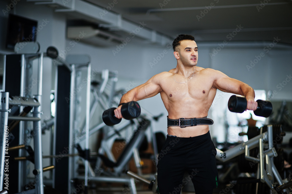 Muscular arab man training in with dumbbells modern gym. Fitness arabian men with naked torso doing workout . Muscular arab man training in with dumbbells modern gym. Fitness arabian men with naked torso doing workout .