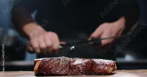 Chef sharpening his knife in front of raw steak. Chef preparing his cooking knife for cutting meat on kitchen table
