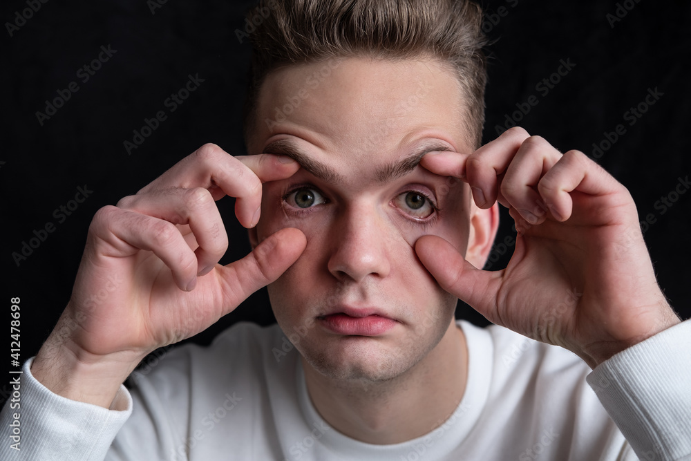 young guy, tired sleepy student opens his eyes with his hands