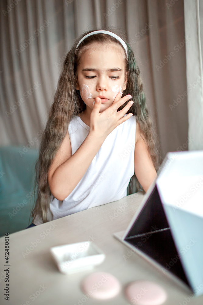 Beautiful teenage girl watching beauty master class with tablet online and doing spa procedure by herself, kid with smooth mask on face, beauty salon at home Beautiful teenage girl watching beauty master class with tablet online and doing spa procedure by herself, kid with smooth mask on face, beauty salon at home