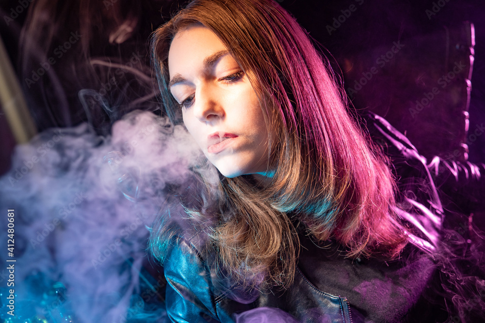 A blower blows smoke. Vaper blows smoke from his lips. Woman lets out smoke from her mouth. Concept is the pleasure of smoking. A student smokes an electronic cigarette. Vaper on a dark background A blower blows smoke. Vaper blows smoke from his lips. Woman lets out smoke from her mouth. Concept is the pleasure of smoking. A student smokes an electronic cigarette. Vaper on a dark background