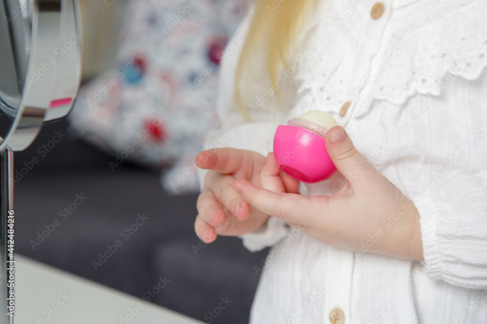 Adorable toddler girl with lip balm in front of mirror.