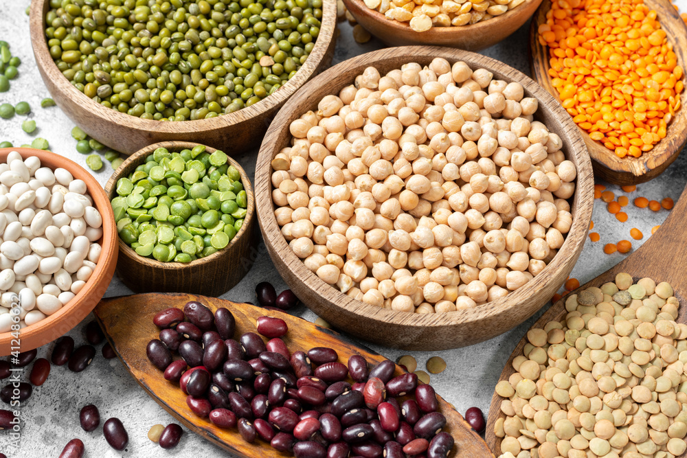 Different legumes. Mung beans, red and white beans, lentils, peas and chickpeas in wooden bowls on the light grey kitchen table. Beans closeup. Vegetarian food