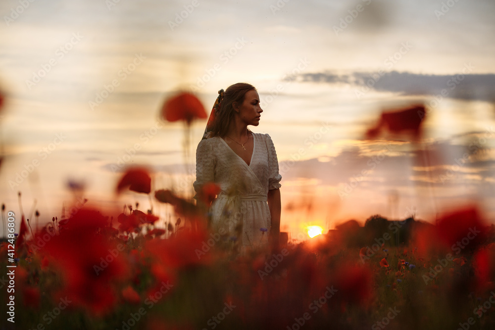 girl in a white dress in a field of poppies on a sunset background