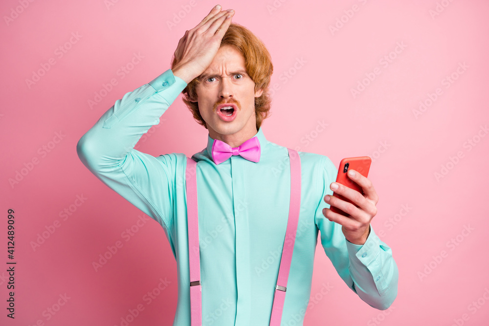 Photo of young questioned uncertain shocked amazed man sees fake news in phone isolated on pink color background Photo of young questioned uncertain shocked amazed man sees fake news in phone isolated on pink color background