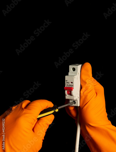 Electrician hands with gloves connect cable to Miniature Circuit Breaker with screwdriver photo