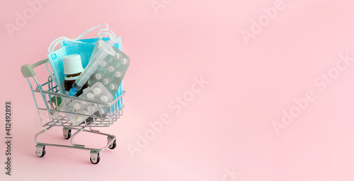 Concept of Vaccination against viruses.Medicines, syringes, pills and masks in a small shopping cart on pink background.