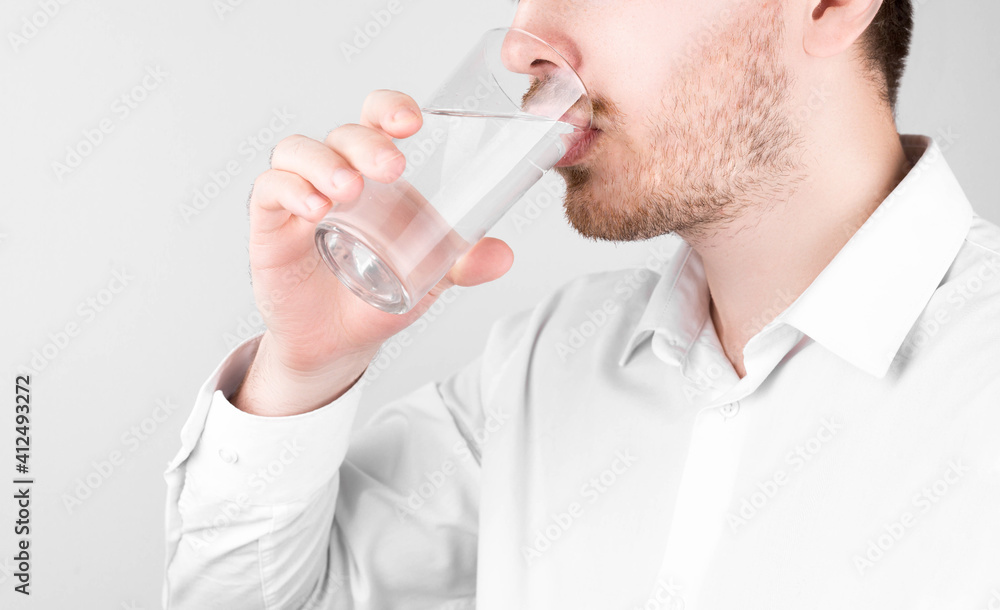 Man in shirt holding a glass of water. Health care concept. Fresh water. Young man. A man in a T-shirt. Ecology concept. The man in the room. Healthy drink concept. Holding glass in hand. Man in shirt holding a glass of water. Health care concept. Fresh water. Young man. A man in a T-shirt. Ecology concept. The man in the room. Healthy drink concept. Holding glass in hand.
