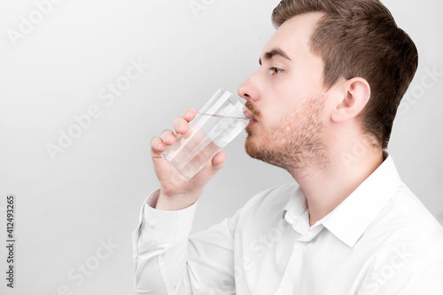 Man in shirt holding a glass of water. Health care concept. Fresh water. Young man. A man in a T-shirt. Ecology concept. The man in the room. Healthy drink concept. Holding glass in hand.