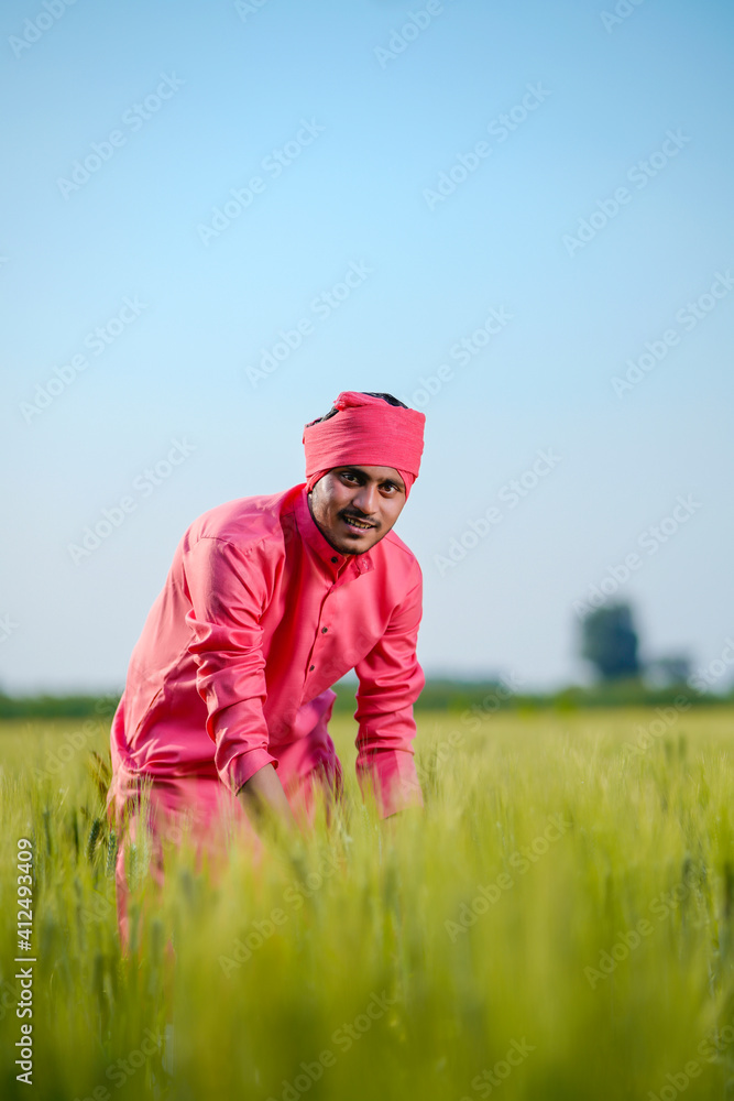 Young indian farmer standing at green wheat field on sky background Young indian farmer standing at green wheat field on sky background