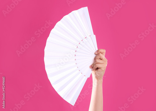 Woman holding white hand fan on pink background, closeup photo
