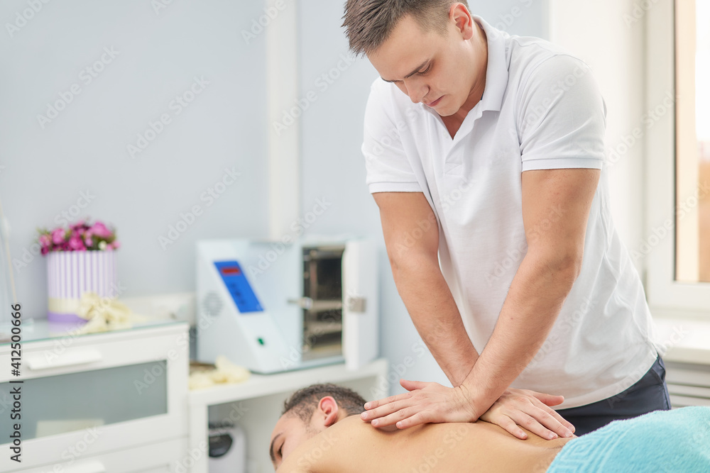 Fototapeta premium Close-up of a physical therapist massaging the back of a man in a medical office. Rehabilitation therapy for the back.