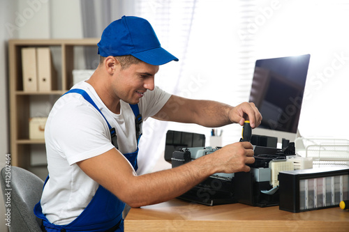 Repairman with screwdriver fixing modern printer in office