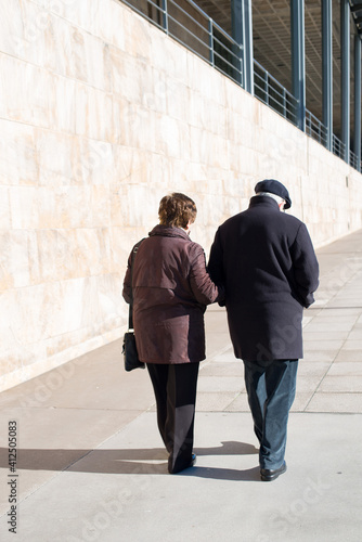 Aged couple over70 seen from the back walking away on an empty street in a sunny day. Concept social distance covid 19