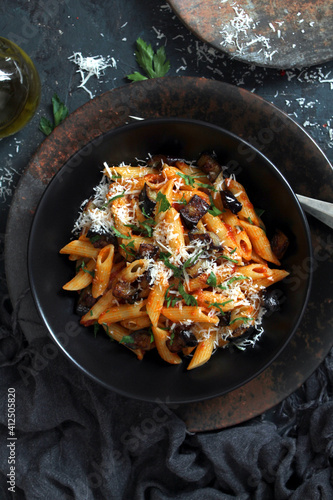 Pasta alla norma - Italian pasta with eggplant, tomato and parmesan cheese on dark table. Top view with copy space.