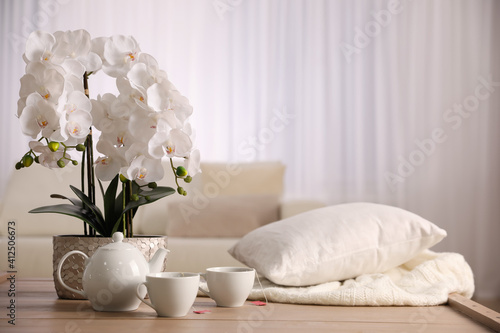 Beautiful orchid, teapot and cups of tea on table indoors