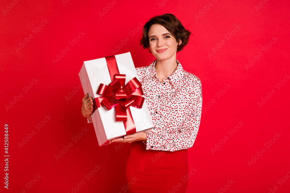 Portrait of attractive cheerful brown-haired girl holding in hands gift festal occasion isolated over bright red color background Portrait of attractive cheerful brown-haired girl holding in hands gift festal occasion isolated over bright red color background