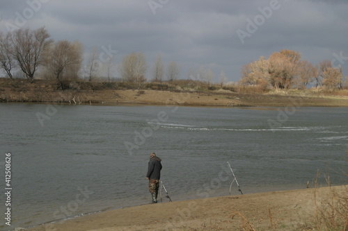 A lone fisherman on the river bank with fishing rods in bad weather.