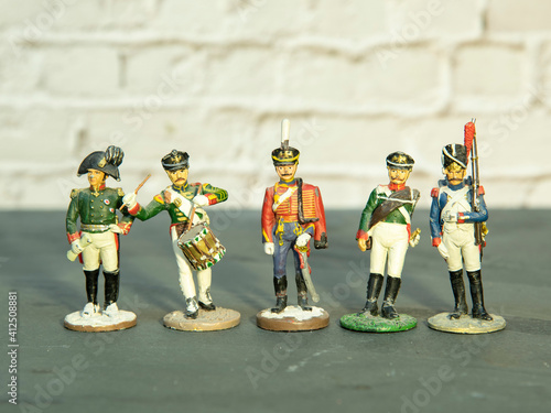 A few miniature tin soldiers stand on a gray surface against a brick wall.