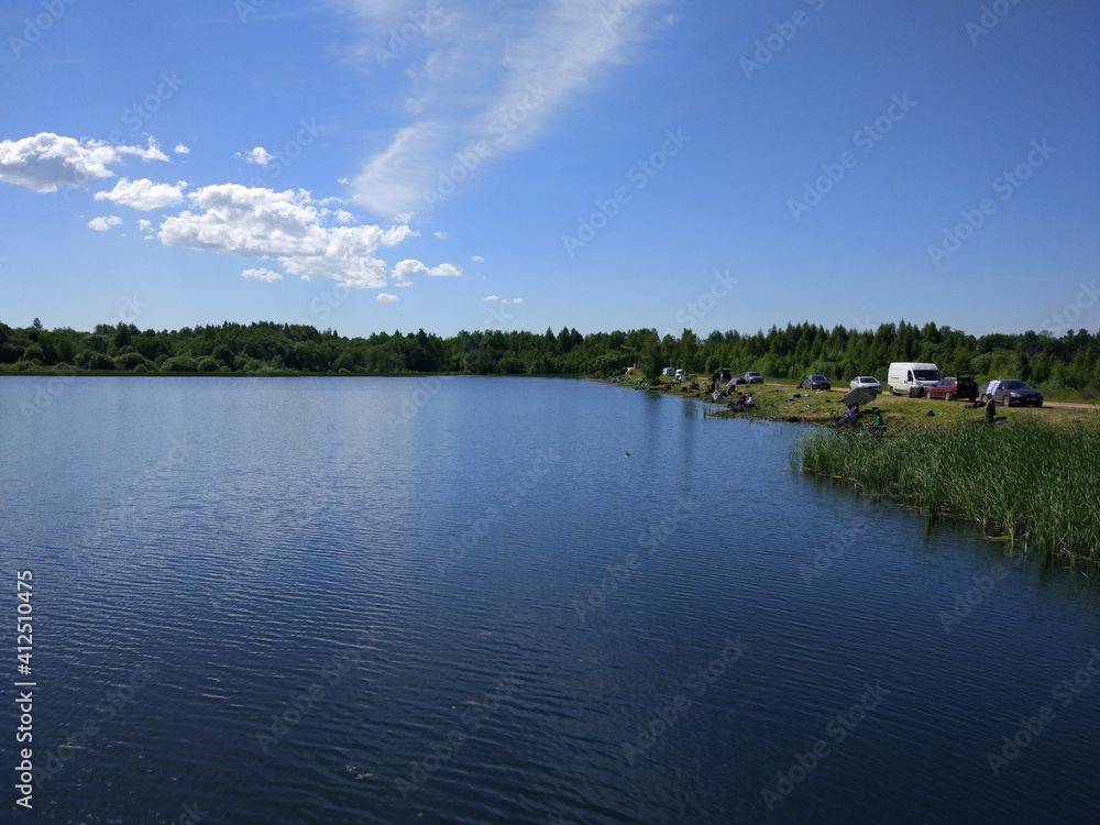 The calm surface of the lake surrounded by forest with fishermen on the shore. The calm surface of the lake surrounded by forest with fishermen on the shore.