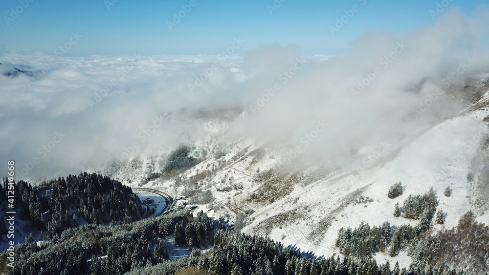 Snow forest in the mountains, above the clouds. View from above, from the drone. Coniferous trees are covered with snow. Clouds float along the gorge. Snowy hills and Sunny day. Tourists in mountains Snow forest in the mountains, above the clouds. View from above, from the drone. Coniferous trees are covered with snow. Clouds float along the gorge. Snowy hills and Sunny day. Tourists in mountains