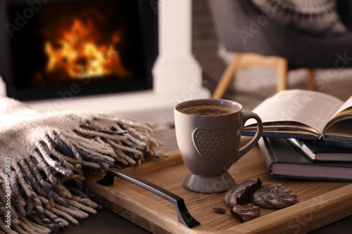Quadro su tela Cup of coffee, broken cookie and books on wooden table near fireplace indoors