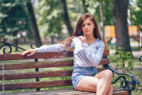 Sexy young woman sits on a wooden bench in a city park.