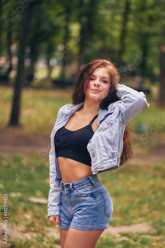 young woman in a city park. shorts, a top, a denim jacket, loose long hair. vertical