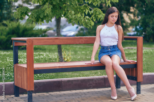 A woman sits on a park bench and looks at her shoes.