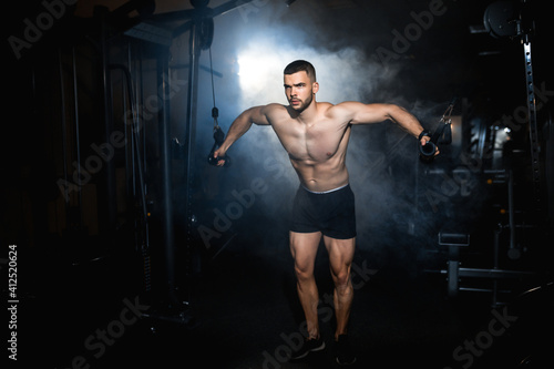 Young sportsman doing pectoral muscle exercise in the gym. Atmosphere smoke