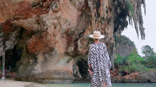 woman walks at Krabi lagoon, she walking on sandy beach in tunic, against magnificent mountains photo